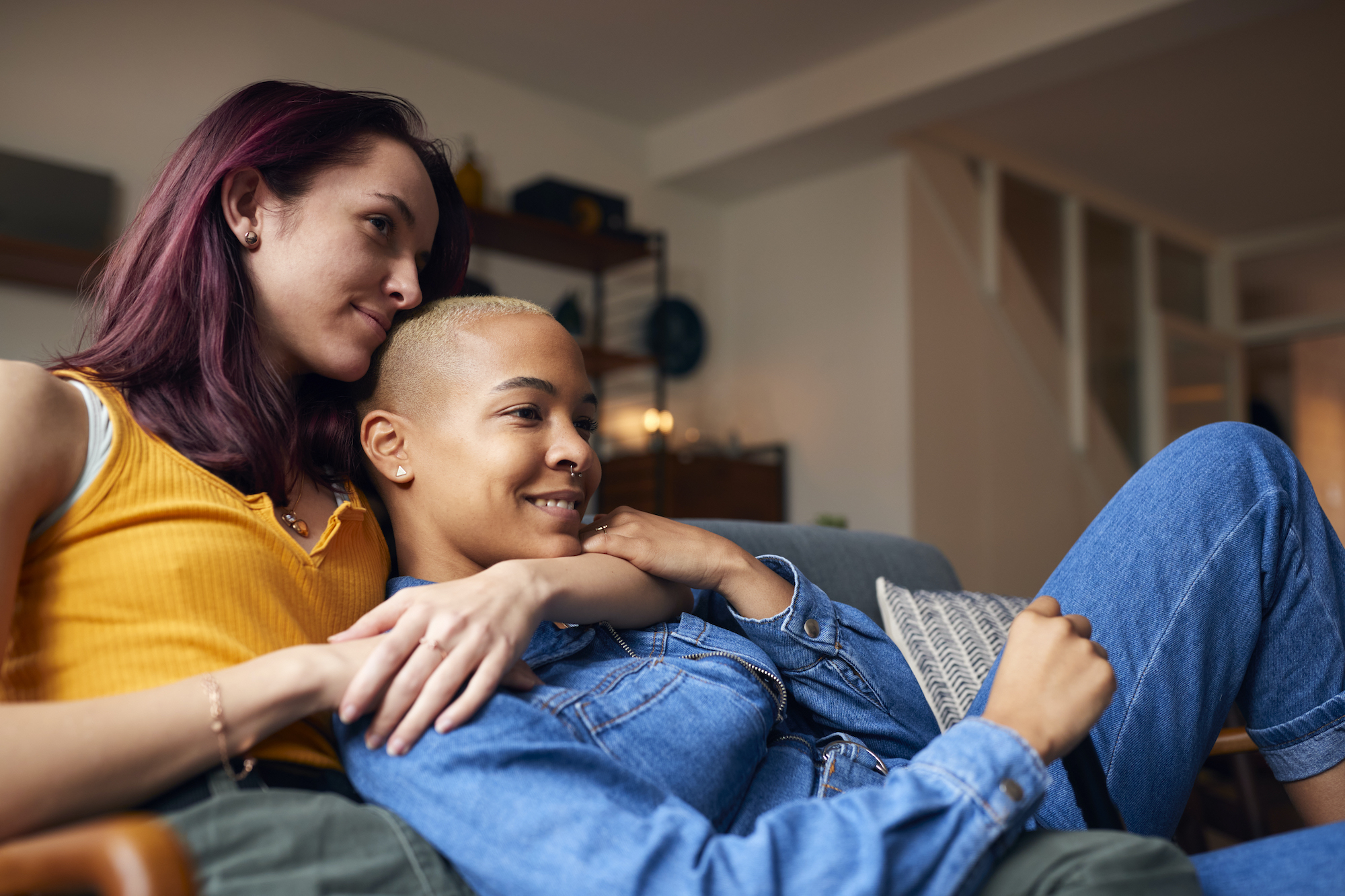 Loving Same Sex Female Couple Lying On Sofa At Home Watching TV And Relaxing Together Same sex female couple sitting on sofa and relaxing