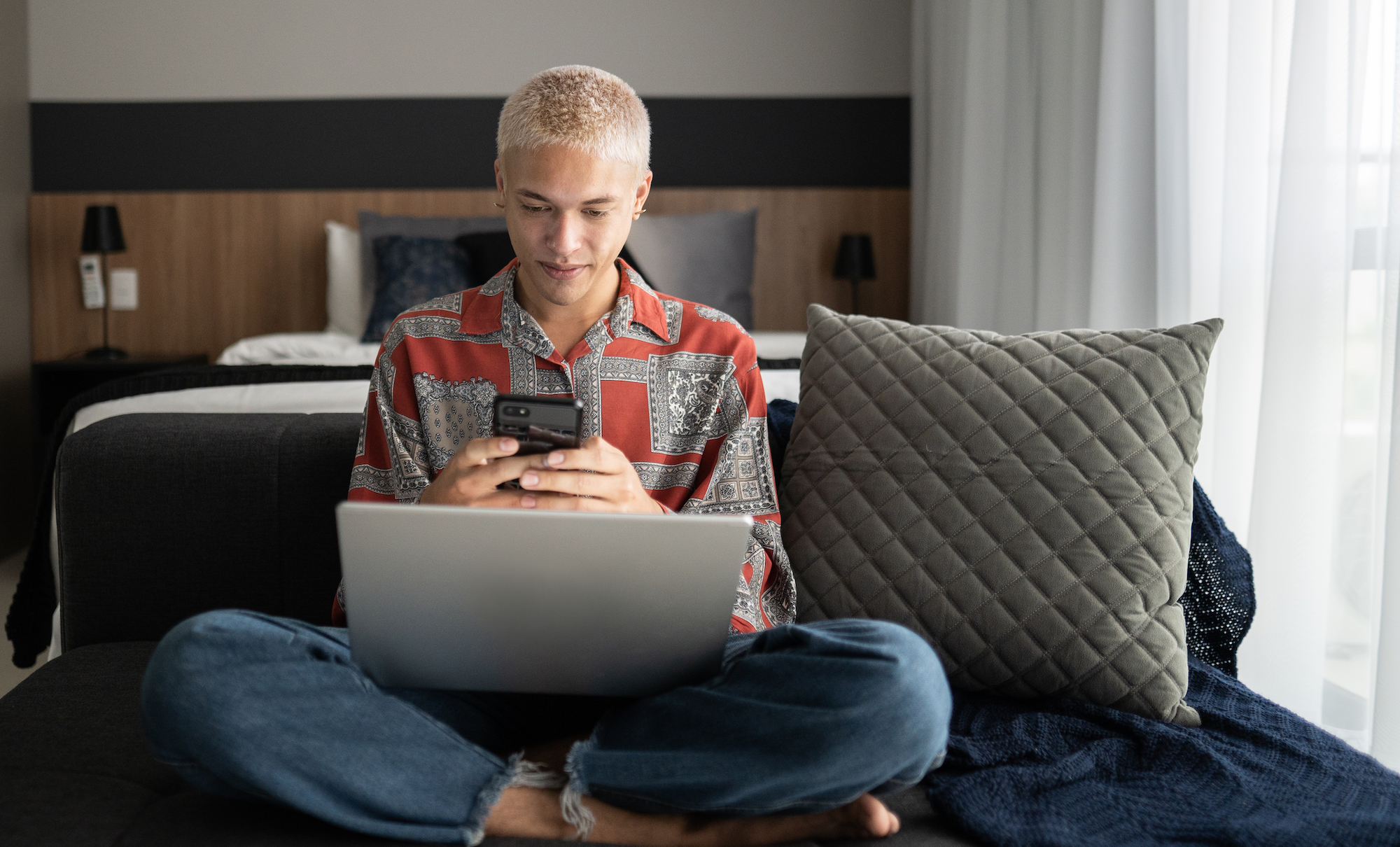 Young man using smartphone and laptop at home Gen Z young man using phone and laptop at home