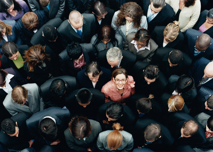 Businesswoman Looking up at Camera and Standing Outdoors Surrounded by a Large Group of Business People